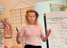 Donna teaching a class with a skeleton and easel nearby.